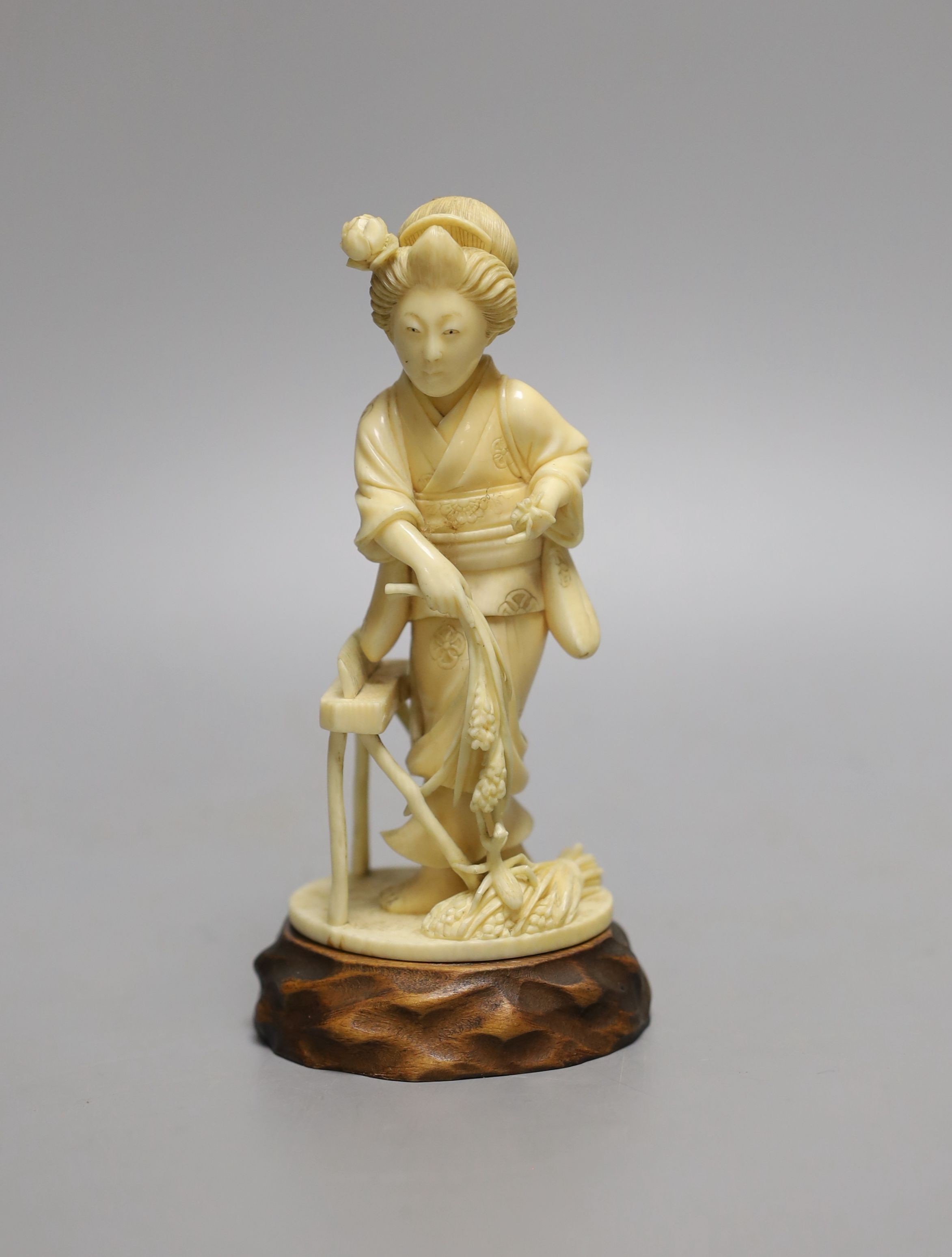 A Japanese Tokyo school carved ivory figure of a woman flailing wheat, Meiji period, wood stand - 14.5cm tall (including stand)